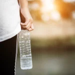 Rainwater marka su şişesi tutan sporcu, sabah güneşi arka planda, açık hava sporları için ideal su çözümü.